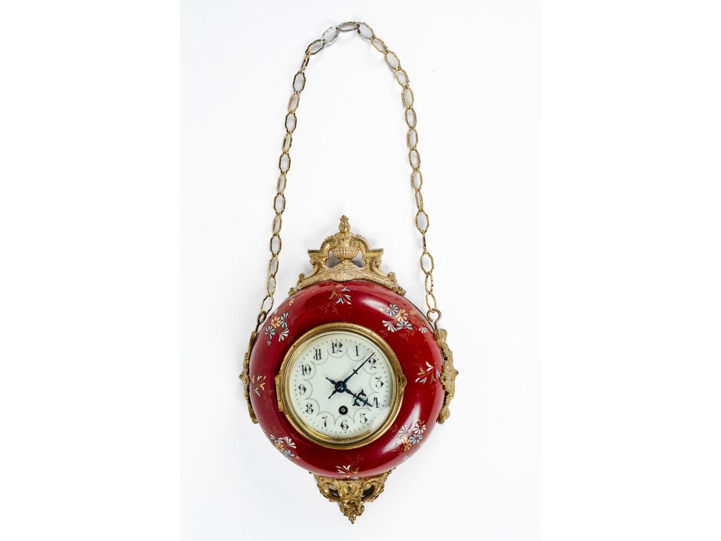 Petite pendule murale en faïence fine à décor émaillée de petites fleurs et dorures présentée sur une monture en bronze doré avec chainette. Epoque début XXème siècle. Diamètre : 24 cm.