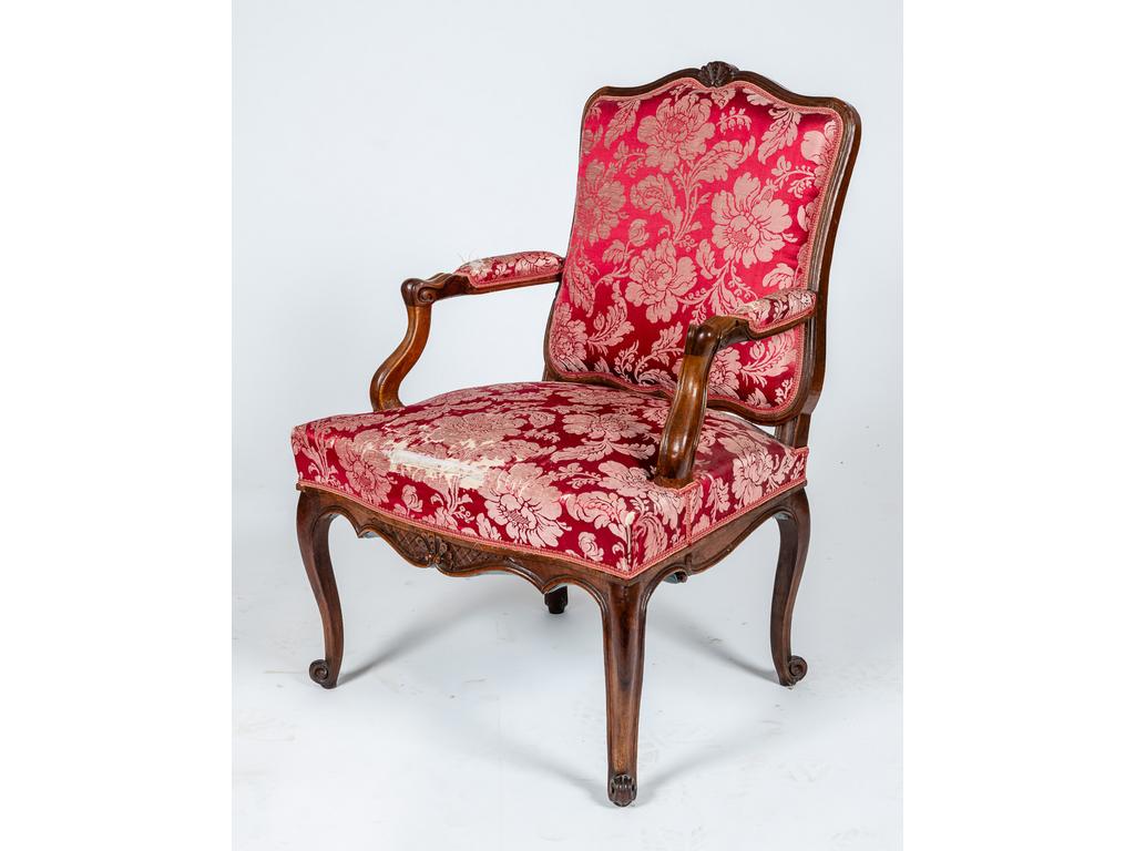 Fauteuil d'époque Louis XV à dossier plat en noyer mouluré et sculpté à décor de coquilles reposant sur quatre pieds à enroulements. Console d'accotoirs à retrait. Garniture de soie rouge. (déchirée)