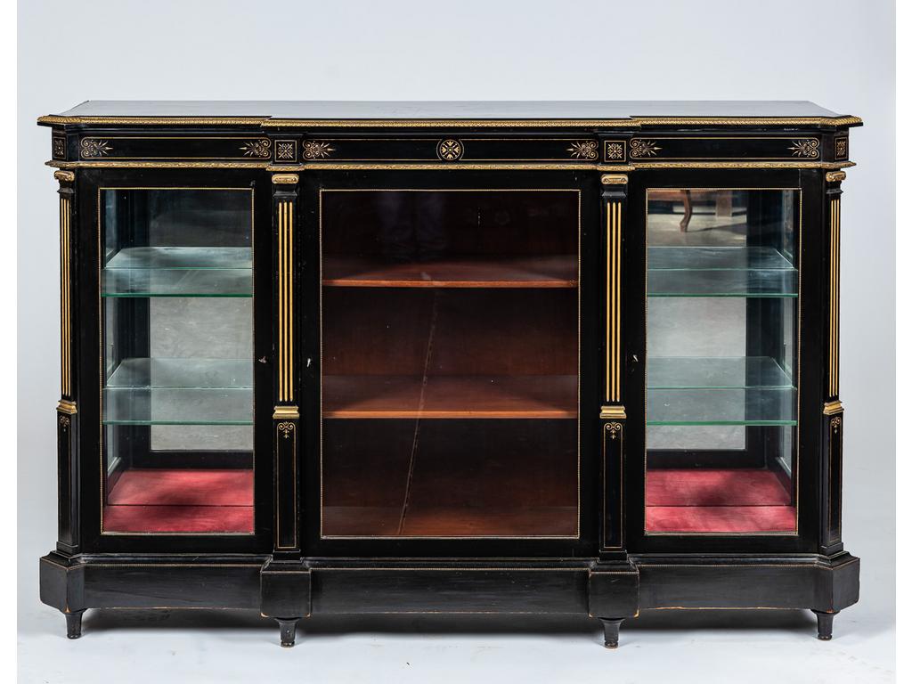 Vitrine basse en bois laqué noir orné de ciselures dorées, baguettes et chapiteaux en bronze. Façade à ressauts ouvrant par trois portes. Epoque fin XIXème siècle. Dim : 102 x 158 x 42 cm.