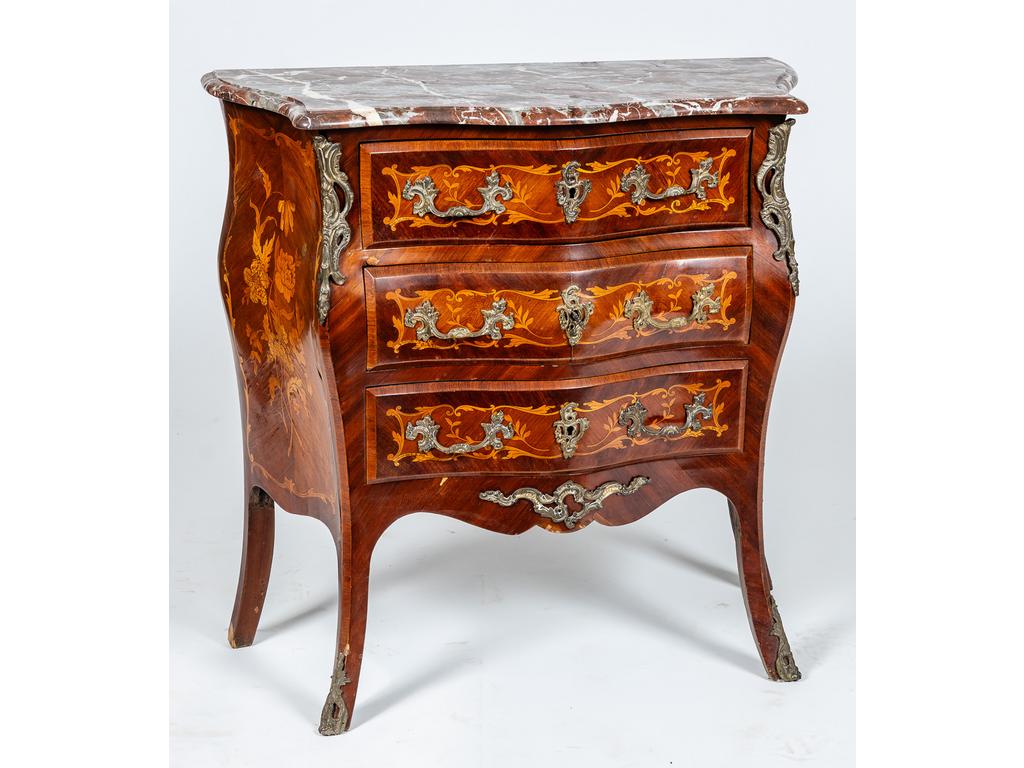 Commode de style Louis XV galbée toutes faces en bois de placage et marqueterie ouvrant par trois tiroirs en façade. Plateau de marbre rouge des Pyrénées. Ornementation de bronze. Epoque 1900. (quelques soulèvements au placage). Dim : 85 x 86 x 40 cm.