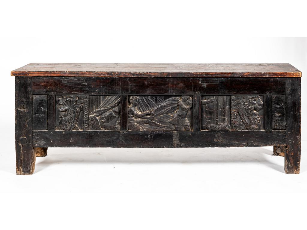 Coffre de style néogothique à décor de trois panneaux sculptés de personnages, mufle de lion et motif. (remontage). Dimensions: 59 x 162,5 x 37,5 cm.