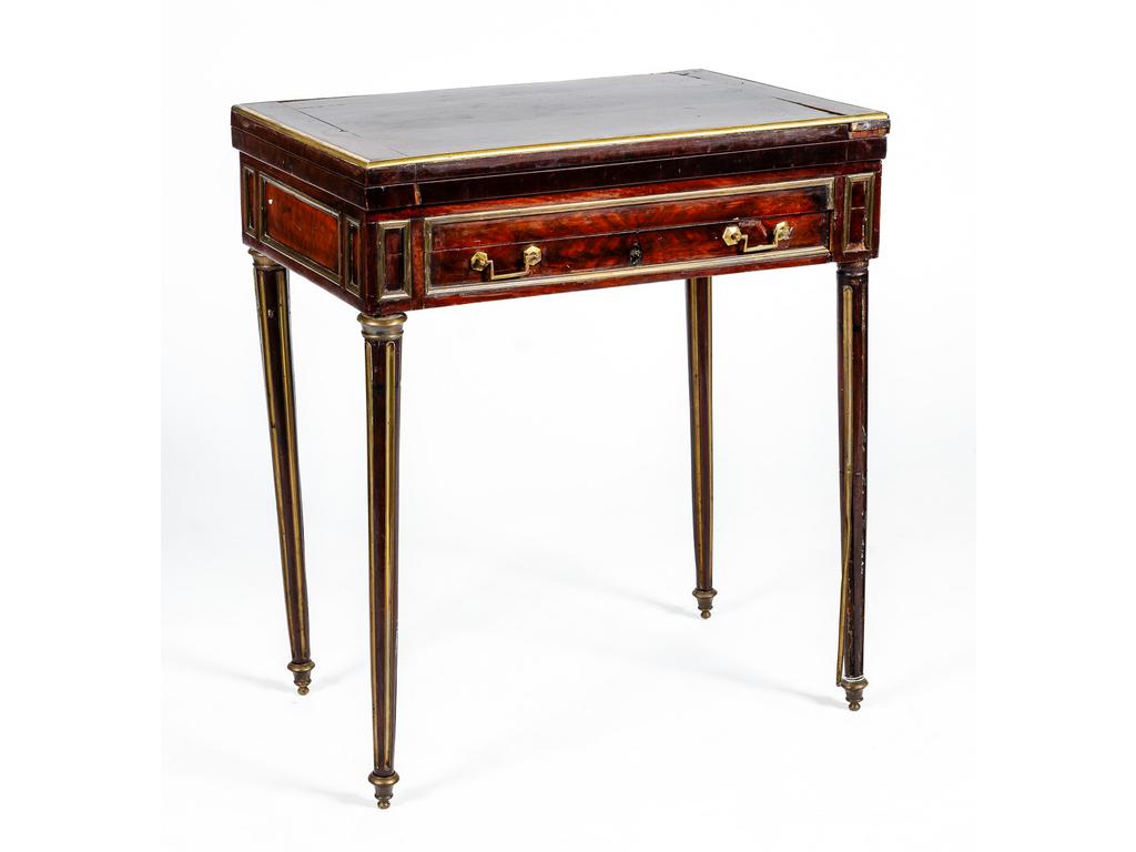 Table à jeux fin d'époque Louis XVI en placage d'acajou à plateau déployant garni de feutre. Elle ouvre par un tiroir en ceinture et repose sur quatre petits pieds cannelés. (Importantes fentes et accidents, à restaurer). Dim : 75 x 64 x 42 cm.