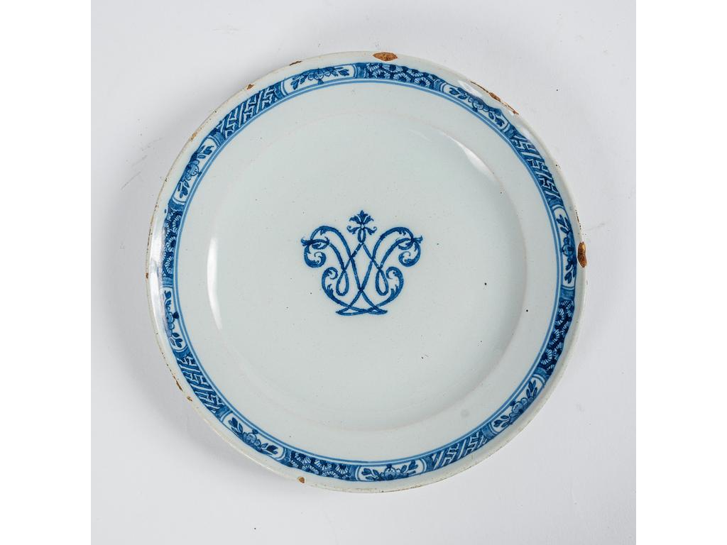 MOUSTIERS : Assiette uniformément ronde en faïence à décor en camaïeu bleu d'un monogramme au centre. (éclat sur l'aile). Epoque XVIIIème siècle. Diamètre : 24 cm.