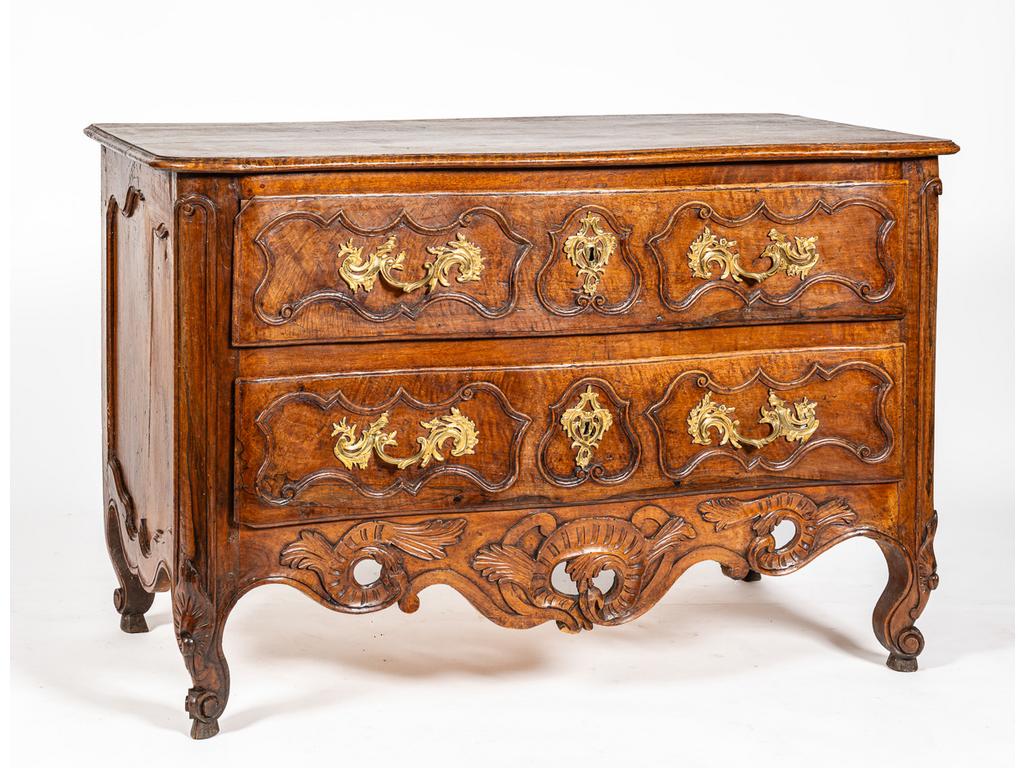 Commode provençale en noyer ouvrant par deux tiroirs en façade légèrement galbée reposant sur quatre pieds galbés et feuillagés reliés par une traverse sculptée et ajourée de coquilles et feuillages. Epoque XVIIIème. (un angle de tiroir cassé). Dim. : 86x132x68cm.