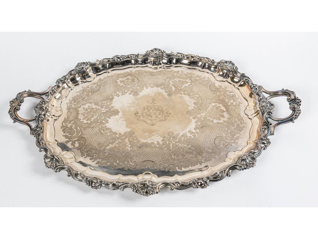 Grand plateau à anses en métal argenté de style rocaille à décor de coquilles et agrafes. Dassin richement ciselé d'un blason dans un entourage de rinceaux, fleurs et treillage. Dim : 80 x 53.5 cm.