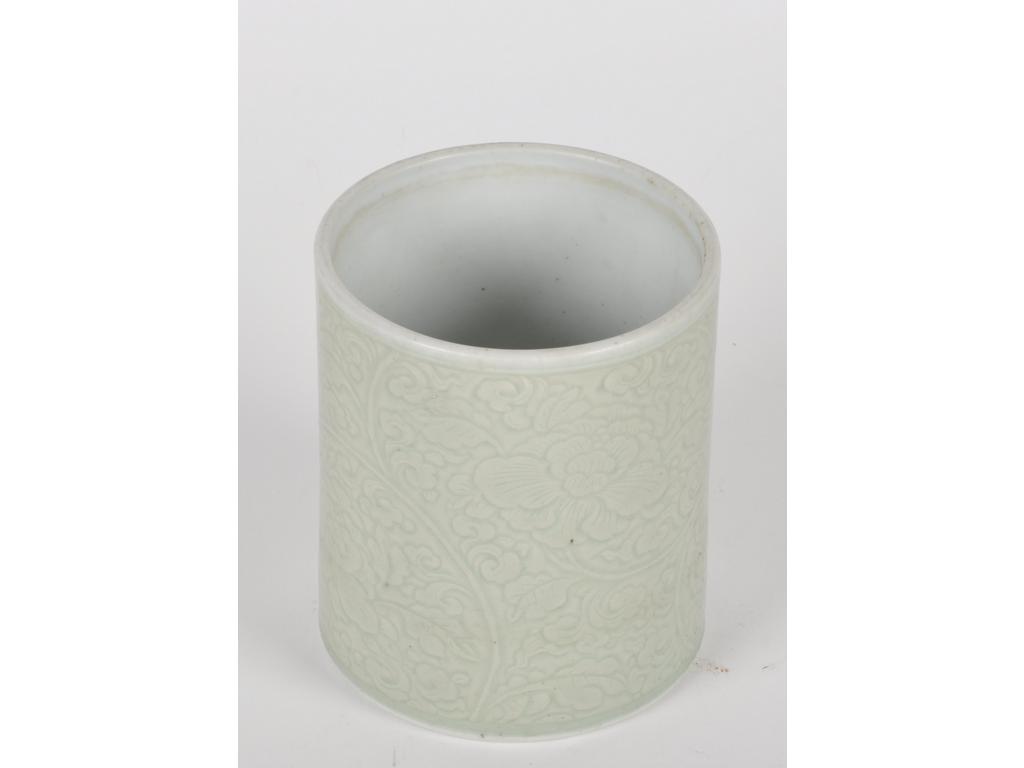 CHINE - Epoque KANGXI (1662 - 1722) : Pot à pinceaux (bitong) en porcelaine émaillée céladon à décor moulé sous la couverte de rinceaux de pivoines épanouies. (Petites égrenures) H. 13,9 cm Diam. 11,8 cm. Expert : Cabinet Portier.