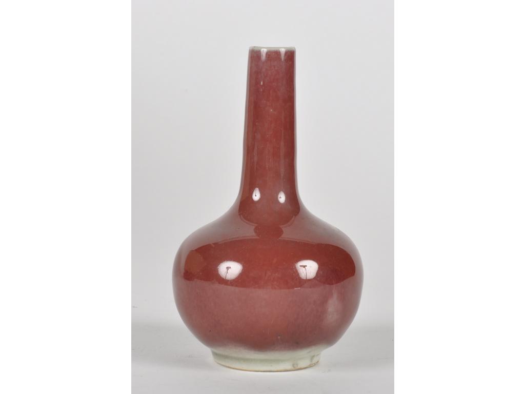 CHINE - XVIIIe siècle : Petit vase bouteille en porcelaine à couverte rouge dite peau de pêche. (Fêlures, fêlure et bulles de cuisson). Hauteur : 12,5 cm. Expert : Cabinet Portier.