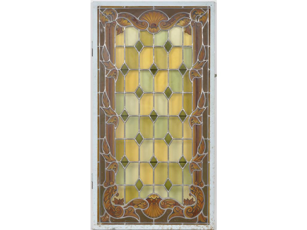 Un vitrail orné en trompe l'oeil d'un encadrement à décor de coquilles et feuillages sur fond jaune d'argent. Dans un cadre en métal laqué avec gonds. Dim totales : 118 x 63 cm. On joint un petit vitrail au motif. Dim totales : 43.5 x 29 cm.