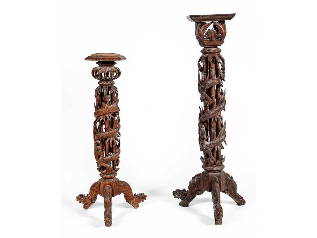 Deux sellettes Extrême Orientales en bois richement ajouré et sculpté de dragons en spirale reposant chacune sur trois pieds (manques des éléments décoratifs sur chacun des deux plateaux, usures et petites restaurations). Hauteurs : 104 et 127 cm.