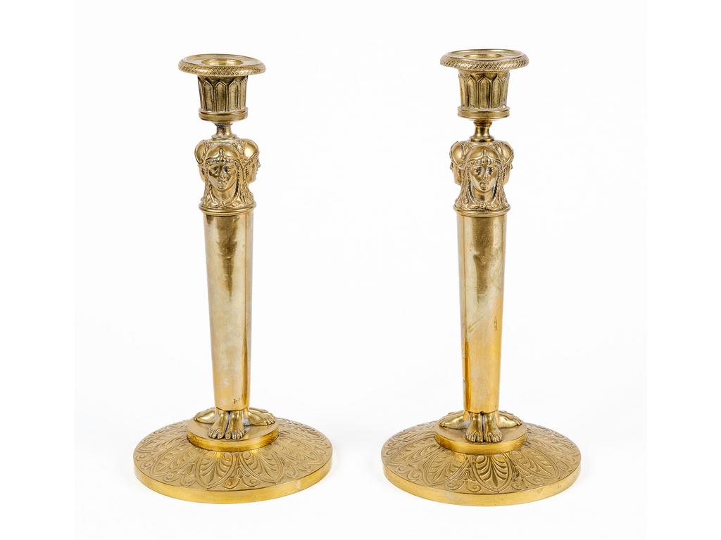 Paire de flambeaux en bronze et laiton représentant trois têtes d'égyptiennes engainées reposant sur une base à décor de palmettes. Epoque Empire. (bobèches à redresser). Hauteur : 28.5 cm.