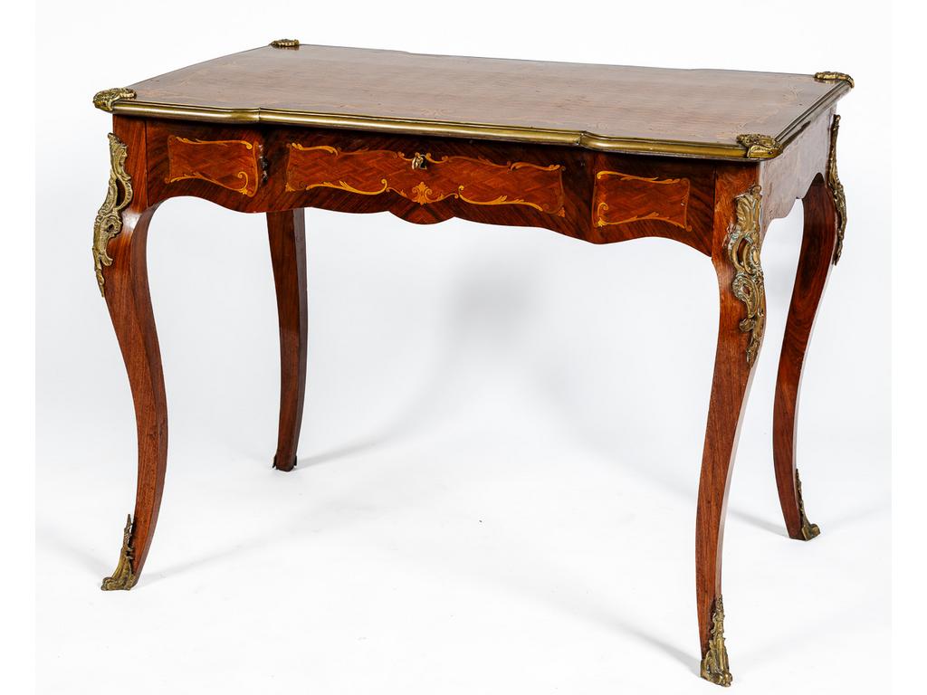 Table à écrire de style Louis XV à décor marqueté de losanges dans des cartouches feuillagés sur fond de palissandre. Elle ouvre par un tiroir en ceinture et repose sur quatre pieds cambrés. Garniture de bronze. Dim : 77 x 101 x 68 cm.