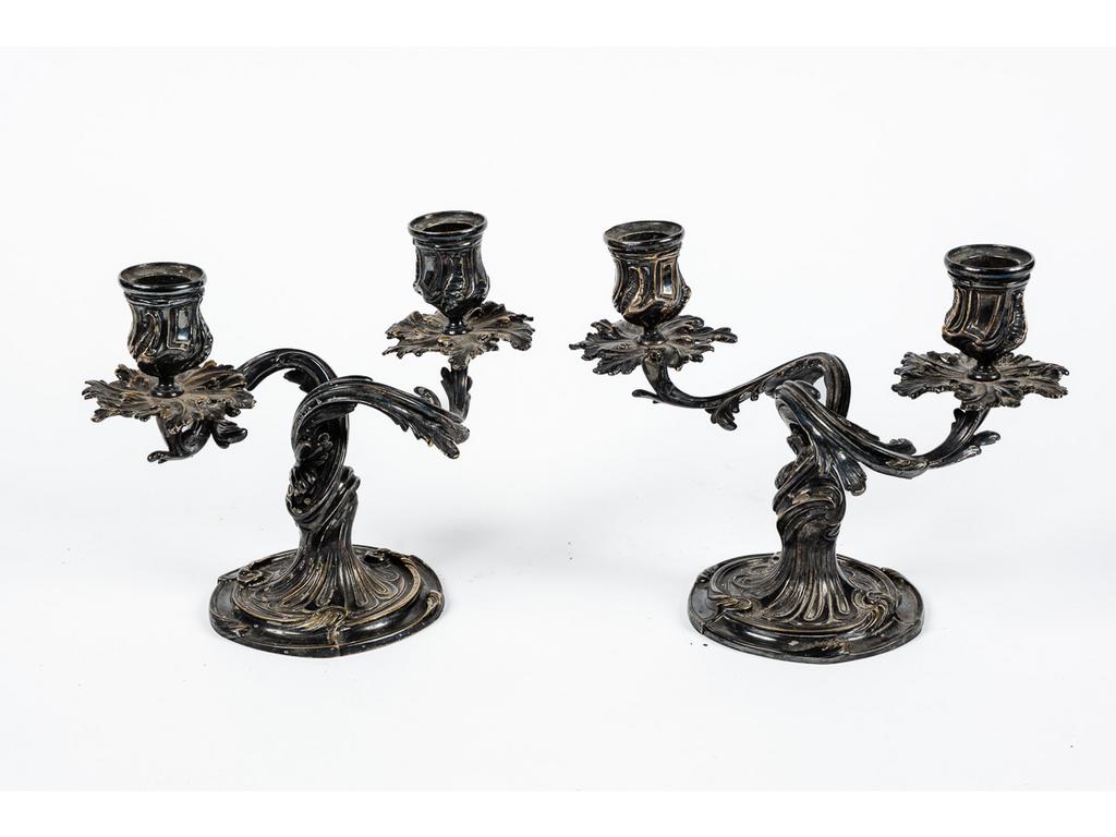 CHRISTOFLE : Paire de flambeaux de style Louis XV en bronze argenté éclairant par deux bras de lumière et à décor mouvementé de végétaux stylisés. Hauteurs : 17.5 cm.
