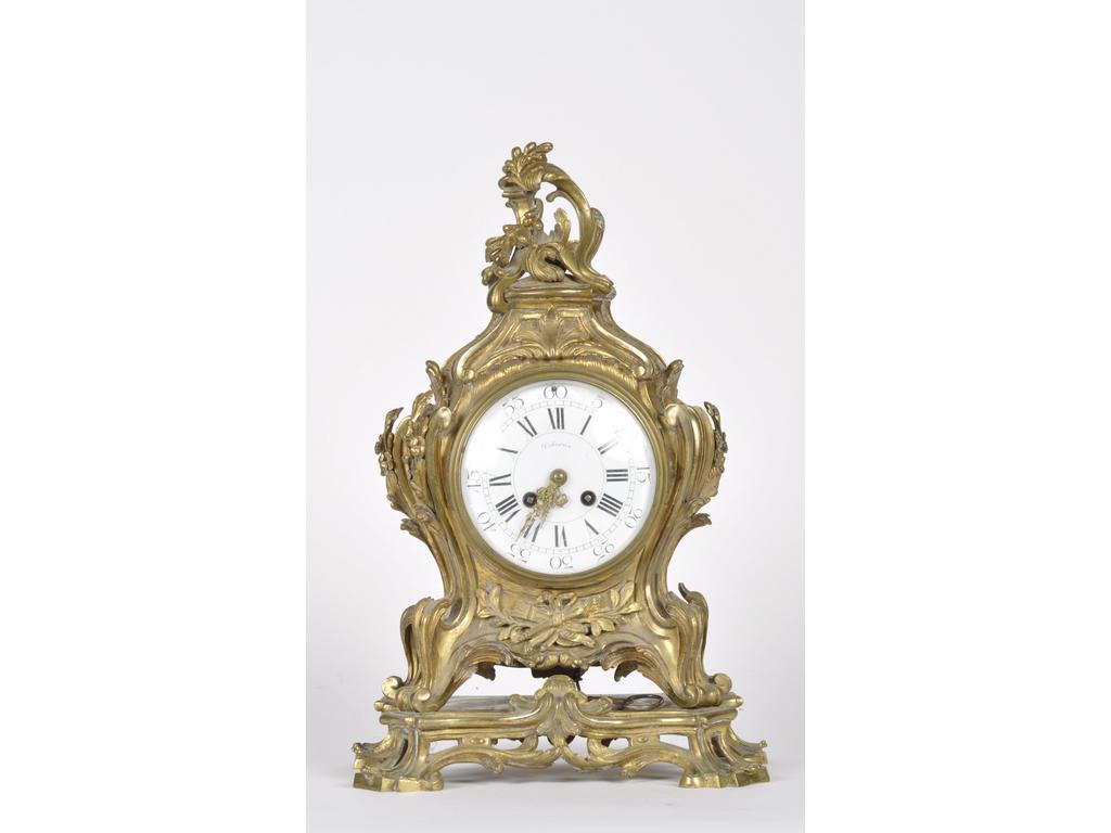 Pendule de style Louis XV en bronze doré à décor de trophée et rinceaux feuillagés. Cadran émaillé à chiffres arabes et romains, signé DELARUE. Hauteur : 43 cm.