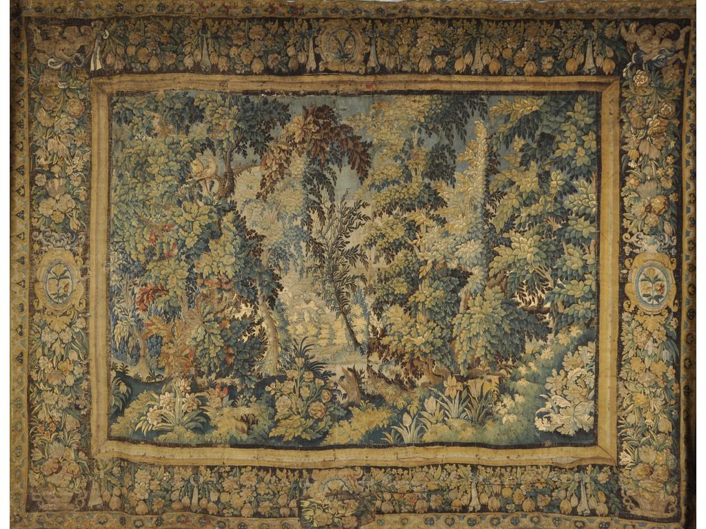 FLANDRES : Importante tapisserie en laine polychrome à décor d'une verdure. Larges bordures ornées de guirlandes de fleurs, de médaillons et de deux angelots aux écoinçons supérieurs. (Tapisserie en mauvais état de conservation, nombreuses reprises et retouches, médaillons sur la marge du bas déchiré et rapiécé. Vendu en l'état). Epoque fin XVII début du XVIIIème siècle. Dim : 340 x 455 cm