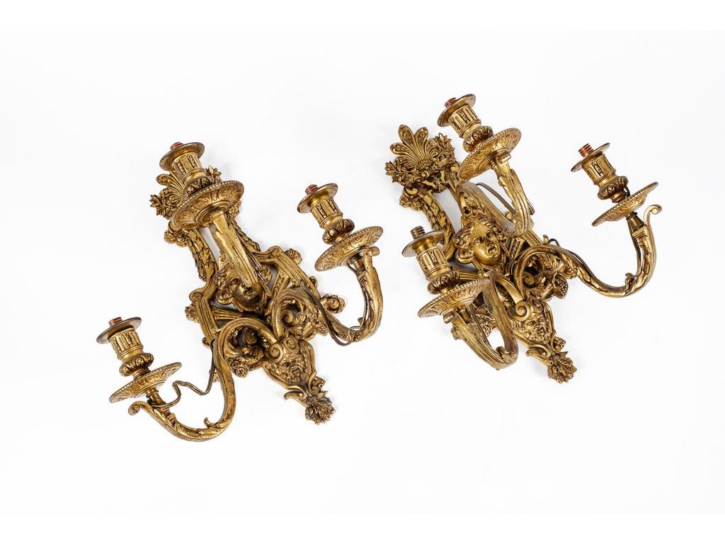 Paire dappliques en bronze et laiton de style Louis XIV éclairant par trois bras de lumière et à décor de lyres, mascarons et plumets. (Manque les bobèches). Monté à l'électricité. Hauteur : 38.5 cm.
