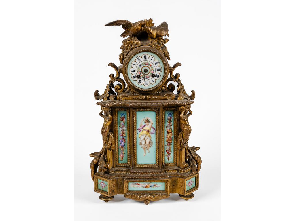 Pendule en métal doré et porcelaine à cadran à chiffres romains signé BERDOU, surmonté d'un couple d'oiseaux et trophées flanqué de deux atlantes engainés. Époque XIXème siècle. Signé DEPREZ. (Manque une aiguille). Dim : 50 x 30 x 15 cm.