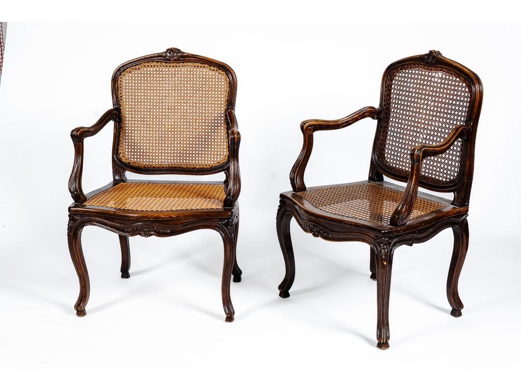 Une paire de fauteuils cannés en noyer mouluré à décor de fleurs et reposant sur quatre petits pieds cambrés. Ancien travail de style Louis XV. (Importantes restaurations et renforts).