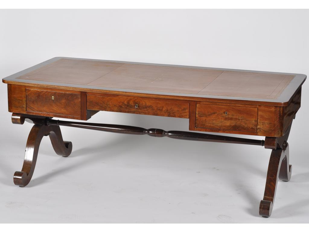 Bureau plat d'époque Restauration en acajou et placage d'acajou, ouvrant en ceinture par trois tiroirs et reposant sur un piétement en X. Plateau gainé de cuir souligné de fer dorés. (restaurations au placage, bureau fabriqué à partir d'un piano-forte transformé). Dim : 74 x 185 x 91 cm.