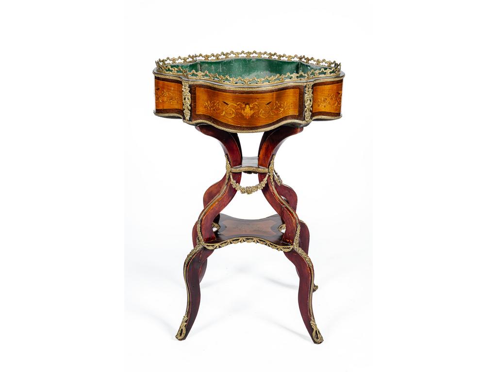 Jardinière d'époque Napoléon III de forme violonnée en bois de placage et trophée. Riche ornementation de bronze et laiton tel que des guirlandes de fleurs en chute, mascarons et galerie. Elle repose sur quatre petit pieds cambrés réunis par une tablette d'entrejambe. Avec sa doublure en zinc. (Petit élément de bronze à refixer). Dim : 82 x 54 x 40 cm.