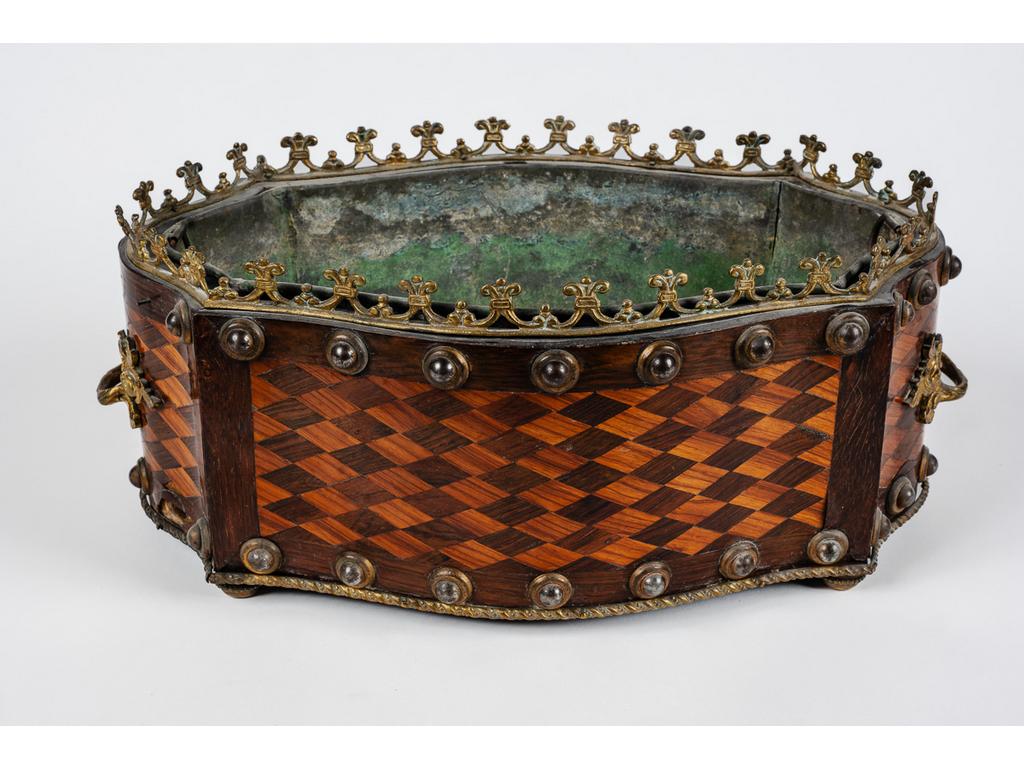 Petite jardinière de table d'époque Napoléon III à décor marqueté en damier de bois de rose et palissandre surmontée d'une galerie en laiton. Ornementation de cabochons en métal doré. Avec sa doublure en zinc. (Soulèvements et manques). Dim : 16 x 40 x 24 cm.