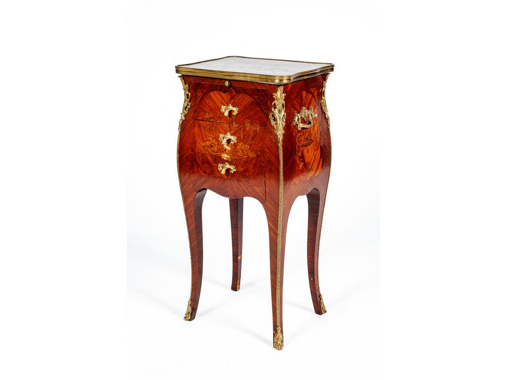 Table de chevet de style Louis XV en bois de placage à décor de paniers fleuris. Elle ouvre par trois tiroirs et une tablette formant écritoire gainé de cuir et repose sur quatre petits pieds cambrés. Garniture de bronze et plateau de marbre à lingotière. (Petites fentes, chocs et manques au placage). Dim : 72 x 34 x 27 cm.