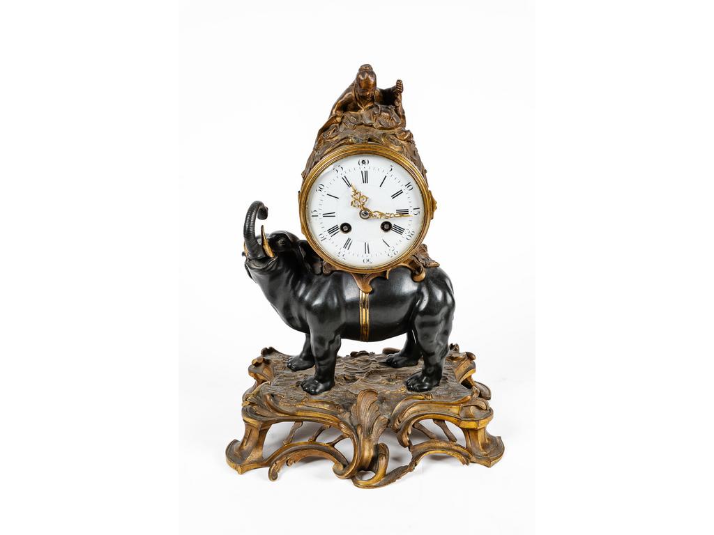 Petite pendule de style Louis XV en bronze patiné et doré, cadran émaillé à chiffres arabes et romains, surmonté d'un chinois et reposant sur un éléphant. Epoque fin XIXème siècle. (Manque l'ombrelle). Hauteur : 38 cm.