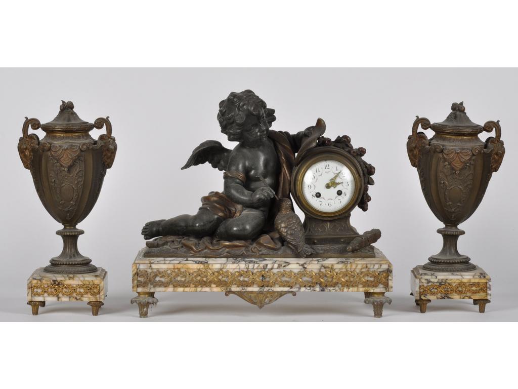 Garniture de cheminée de style Louis XVI en régule et marbre comprenant : Une pendule à l'Amour et une paire de cassolettes. Epoque 1900. (Quelques oxydations). Hauteur de la pendule : 38 cm.