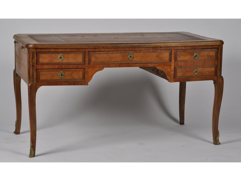 Bureau plat de style Transition et Bibliothèque de style Louis XVI : Bureau plat en marqueterie de bois de rose, ouvrant en ceinture par cinq tiroirs. Plateau et tirettes latérales gainés de cuir. Petite ornementation en laiton. (Manques au placage, plateau tâché). Dim : 75 x 140 x 73 cm. Et la bibliothèque en placage de bois de rose ouvrant par trois portes dont une grillagée. Dim : 176 x 173 x 45 cm. L'ensemble début du XXème siècle.