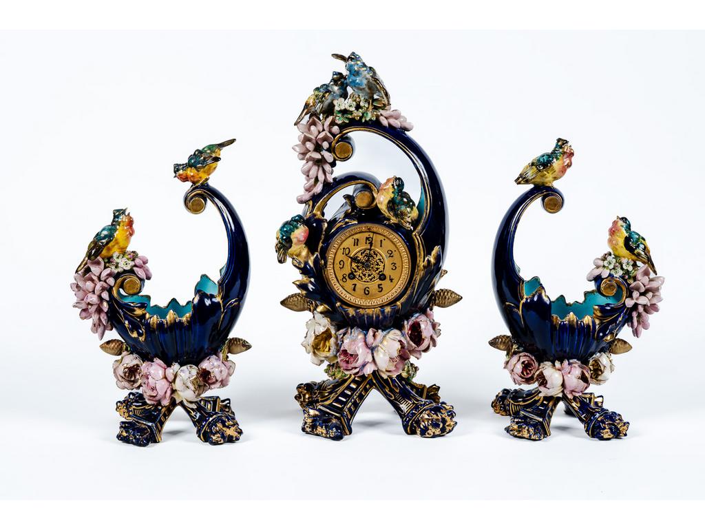 Garniture de cheminée en faïence fine gros bleu à décor en relief de petits oiseaux et de fleurs. Elle comprend : une pendule et une paire de coupes. Hauteur de la pendule : 48 cm. (quelques accidents)