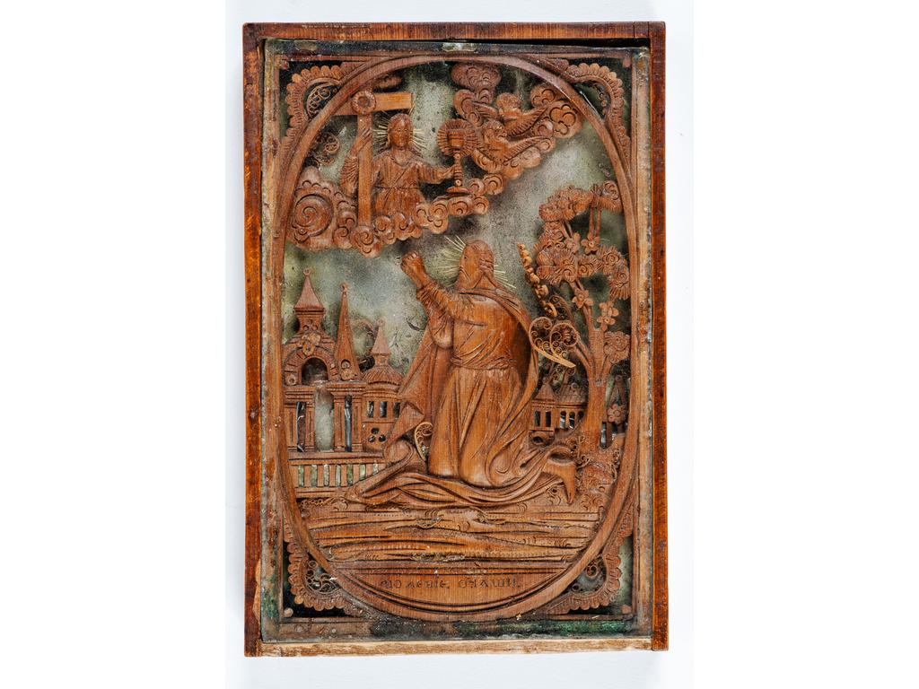 Petit cadre ex-voto en bois sculpté représentant un personnage en prière devant une ville. Dans le ciel, un Saint personnage tenant la Croix et un calice, deux anges dans les nuées sur un fond gris. Epoque Fin  XVIIIème siècle. Dimensions : 15 x 10 cm. (quelques paperoles à refixer)