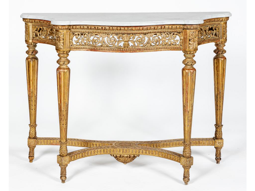 Console de style Louis XVI en bois sculpté et doré. Plateau de marbre blanc reposant sur une ceinture galbée et côtés incurvés. L'ensemble ajouré de rinceaux feuillagés. Reposant sur quatre pieds fuselés, cannelés à entretoise. Epoque XIXème siècle. Dim : 91 x 123 x 46 cm.