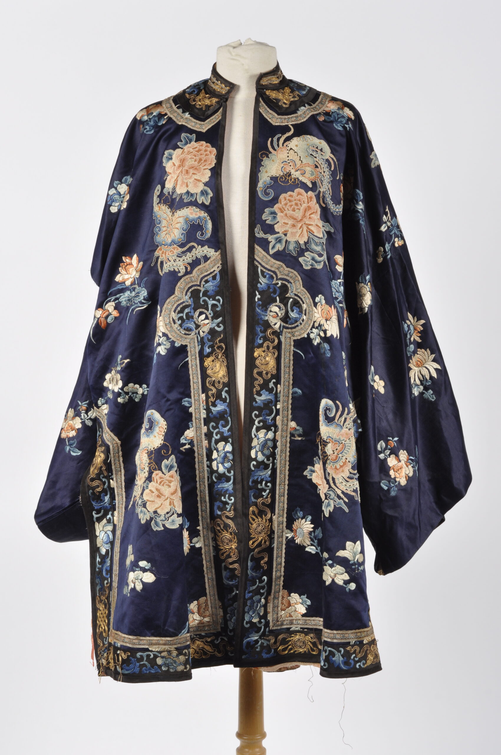 CHINE : Veste en soie bleu-nuit richement brodée de fleurs et papillons en fils polychromes et dorés. Intérieurs des manches également brodés. (accrocs, tâches, une manche à recoudre)