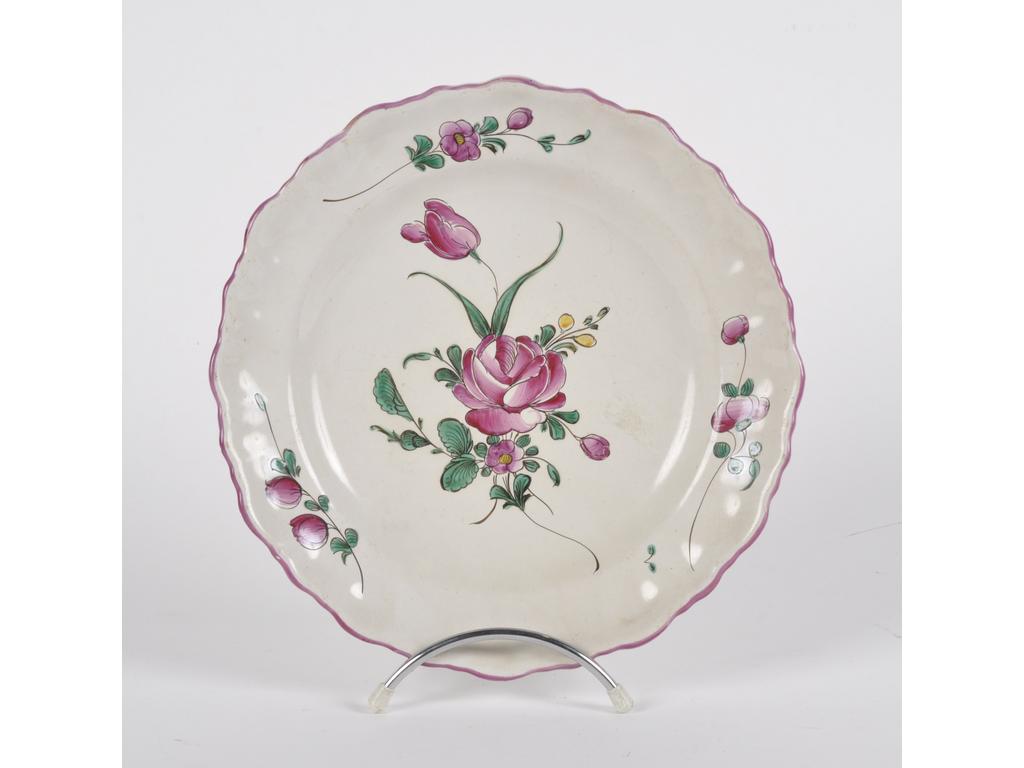 MOUSTIERS, Fabrique de  FERRAT : Assiette en faïence à bords dentelés avec liseré rose à décor peint de fleurs. Epoque début du XIXème siècle. Diamètre : 24 cm.