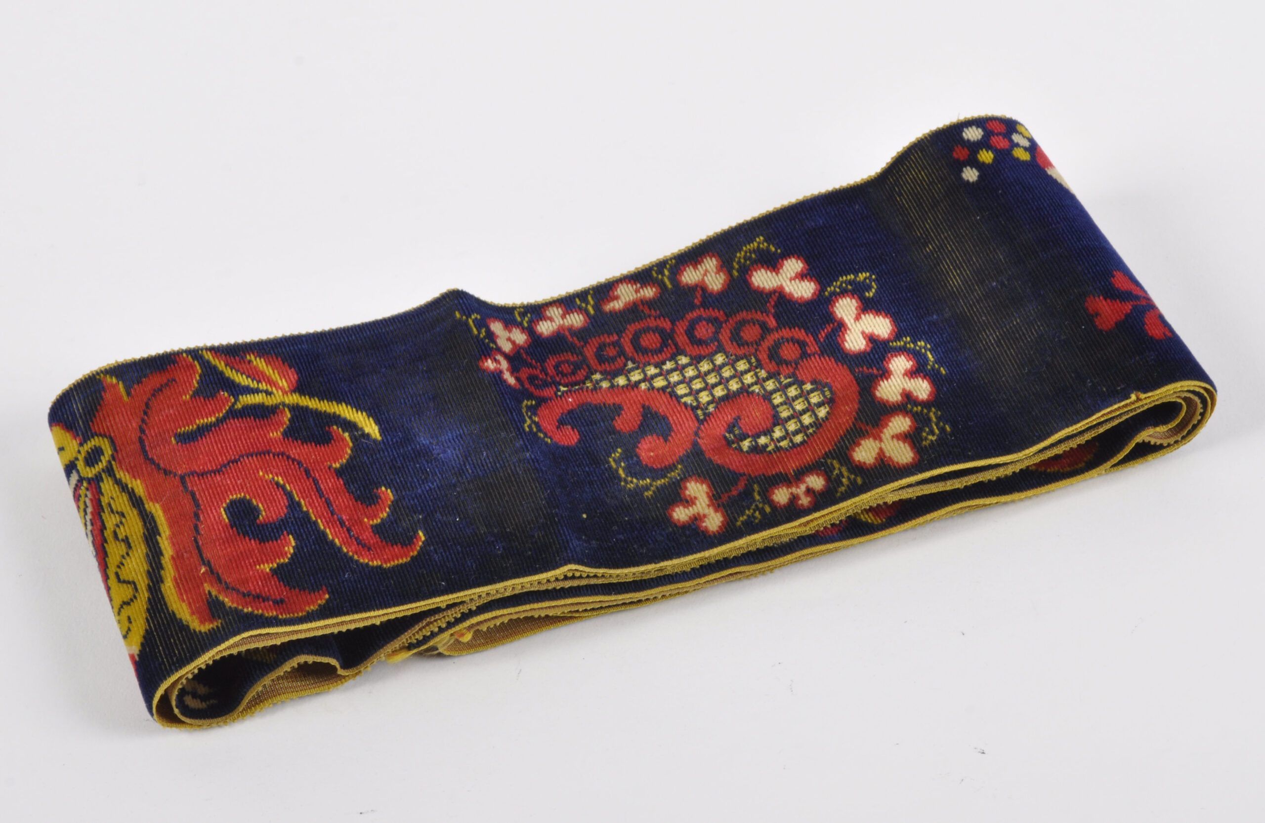 Beau ruban d'Arlésienne en velours à décor de fleurs et de botehs stylisés rouges et jaunes sur fond bleu nuit. Longueur : 148 cm, largeur : 8 cm. (Un fil avec accroc et légères usures sur les bords)