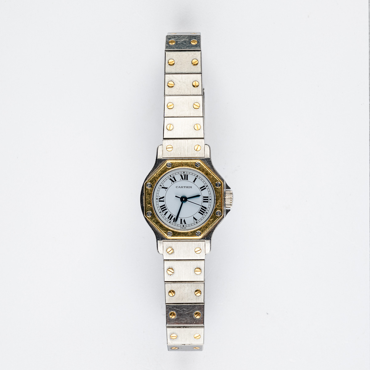 CARTIER : Santos. Vers 1980. Montre-bracelet de dame en or 18k (750) et acier. Boîtier octogonal, lunette en or, signé. Cadran blanc, chiffres romains, minuterie chemin de fer, trotteuse centrale, signé. Mouvement automatique. Bracelet en or et acier. Boucle déployante signée. Diam. 25 mm. Poids brut : 49,00 g. RAPPORT DE CONDITION : Mouvement opérationnel au moment de la rédaction du catalogue. Griffures et rayures d’usage sur la lunette et le boîtier. Couronne de remontoir non d’origine. Boîtier présentant des pas de vis possiblement endommagés, rendant l’ouverture impossible. Un service auprès de Cartier est à prévoir. Veuillez noter que toutes les montres sont vendues en l’état. Aucune garantie sur l’état de fonctionnement. La plupart des montres ont été ouvertes pour identifier le type et la qualité du mouvement, y compris les montres résistantes à l’eau. Il est conseillé à l’acheteur de consulter un horloger pour revoir l’étanchéité de la montre. Les indications données sur l’existence d’une restauration, d’un accident ou sur l’état de préservation restent soumises à l’appréciation personnelle des acquéreurs. L’absence d’indication de pièces de remplacement, d’une restauration ou d’un accident n’implique nullement qu’un bien soit exempt de tout défaut présent. Tous les objets présentés sont susceptibles d’avoir fait l’objet d’un service antérieur et peuvent présenter des pièces non d’origine. Les dimensions et le poids des objets sont renseignés à titre approximatif.