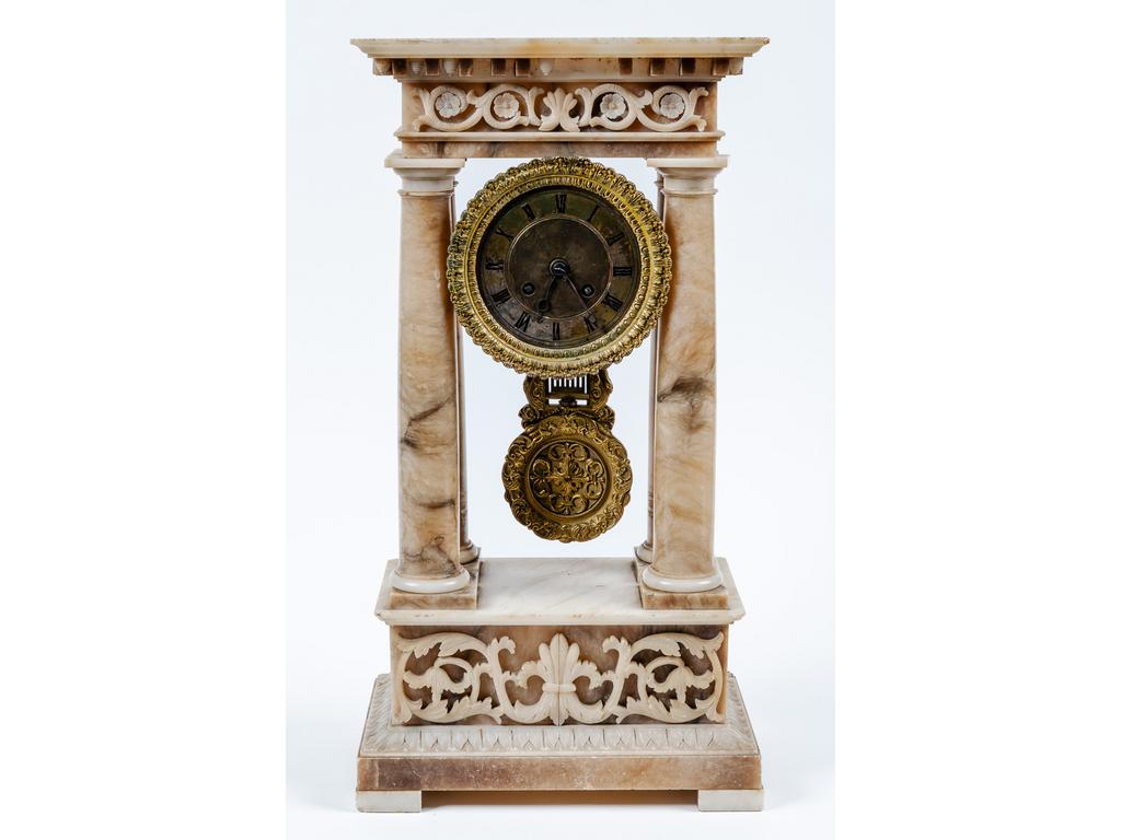 Pendule portique en albâtre à décor de rinceaux feuillagés. Cadran en laiton émaillé à chiffres romains. (Manque la partie supérieure et accidents à la corniche). Epoque XIXème siècle. Dim : 48.5 x 25 x 14.5 cm.