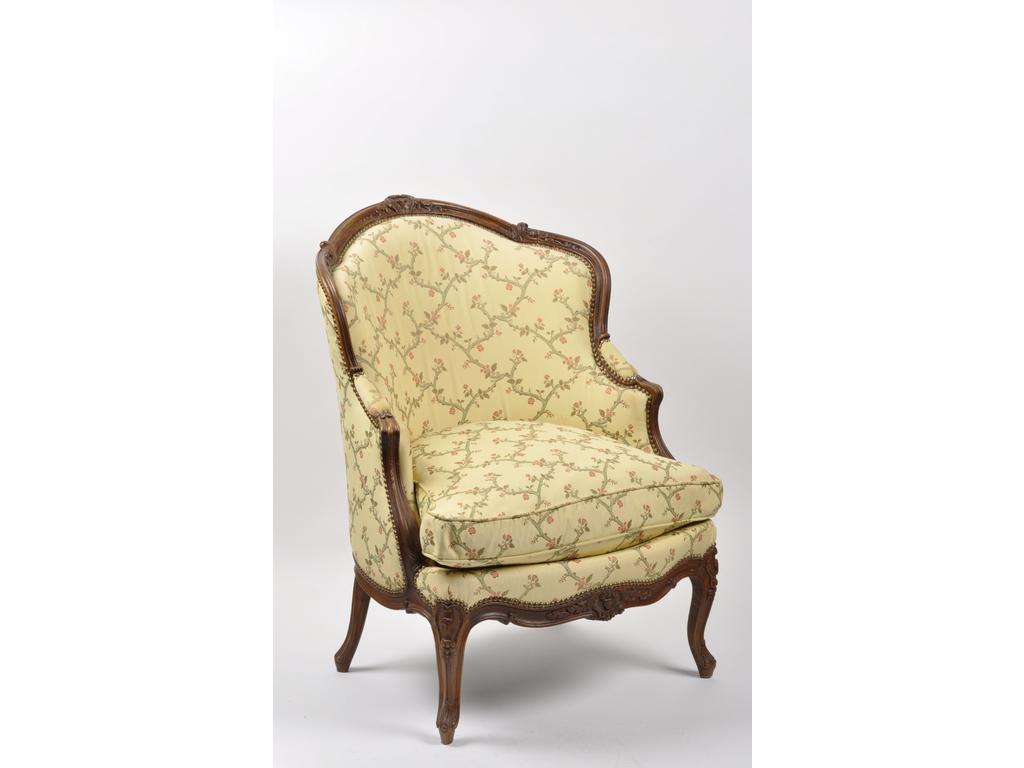 Bergère cabriolet de style Louis XV en hêtre naturel mouluré et sculpté à décor d'un cartouche, rinceaux et agrafes reposant sur un petit piétement cambré. Recouverte d'un tissu jaune à motif fleuri.