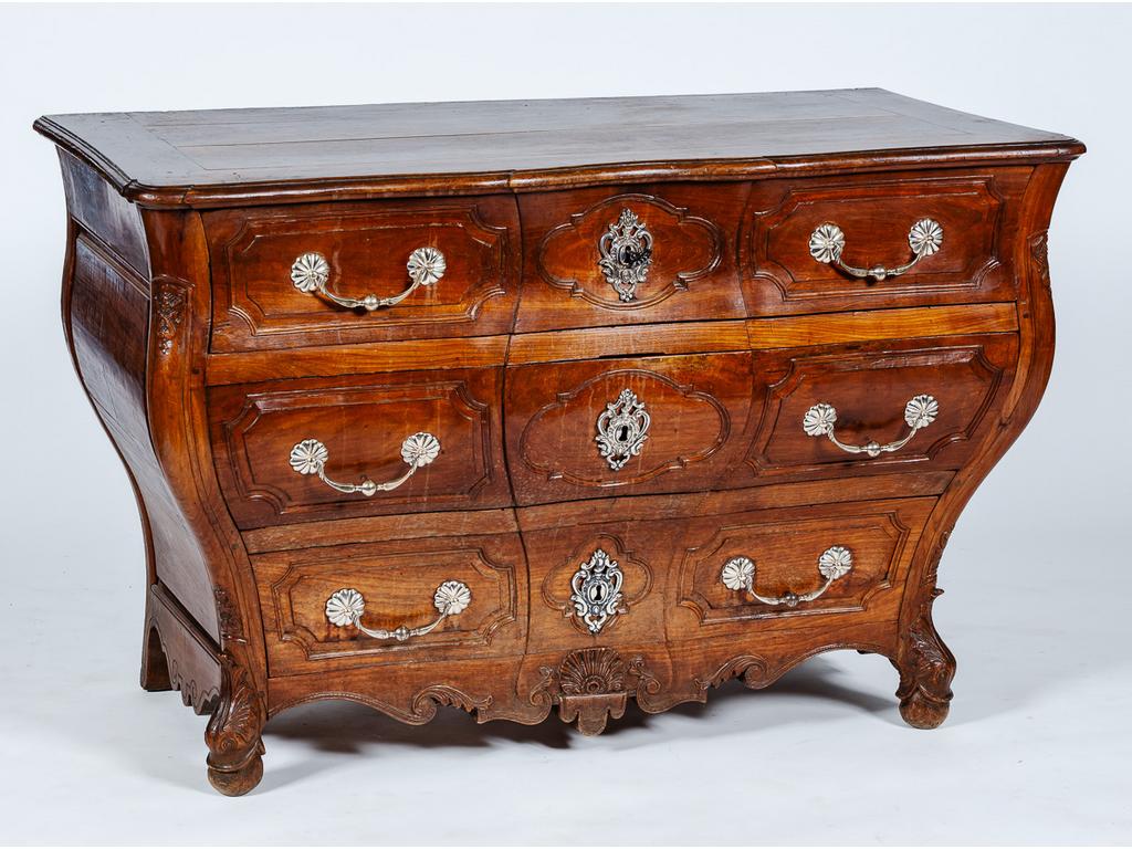 Commode tombeau à léger ressaut en merisier naturel mouluré et sculpté ouvrant pas trois tiroirs en façade, montants cambrés ornés de motifs stylisés et reposant sur un petit piétement à têtes de dauphin relié par une traverse sculptée d'une coquille sur un drapé. Travail de port du XVIIIème siècle. (Poignées de tirage et entrées de serrure remplacées). Dim : 82 x 128 x 69 cm.