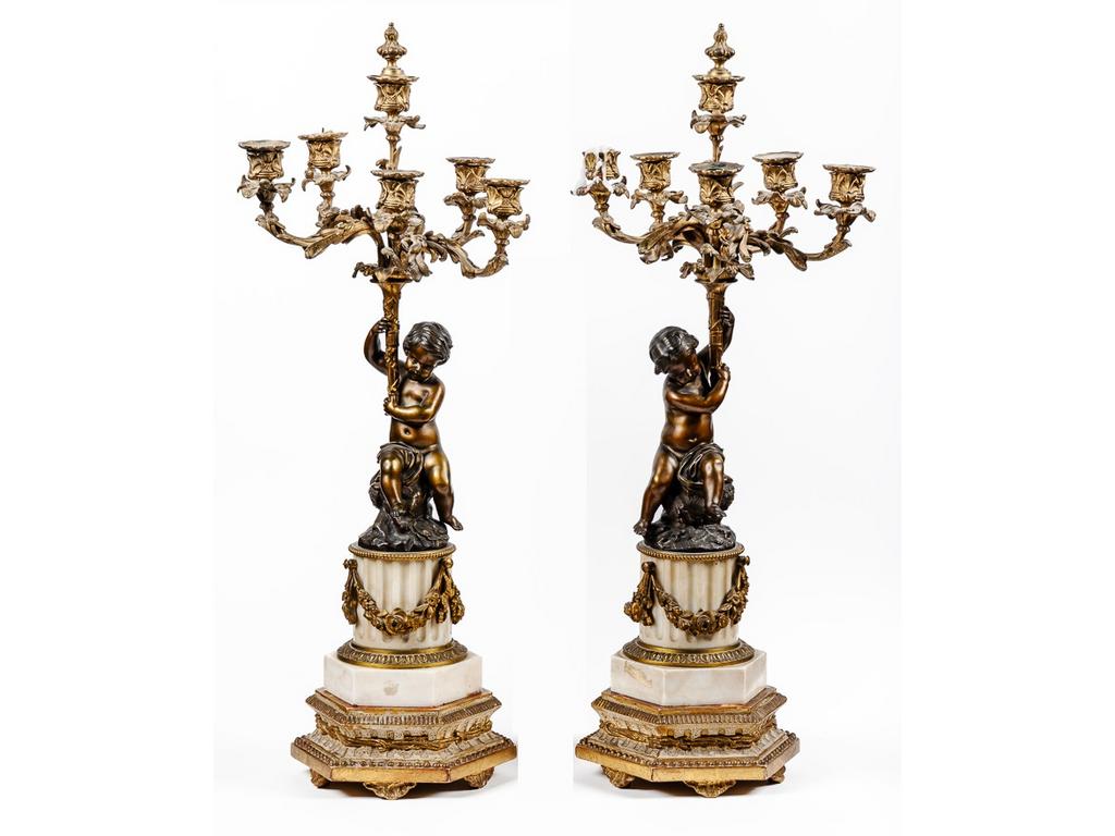 Paire de candélabres en bronze et marbre blanc à décor de putti soutenant une corne dabondance à cinq bras de lumière. Socle à colonne cannelé à décor de guirlandes de fleurs en bronze doré reposant sur une base octogonale. Hauteur : 64 cm.