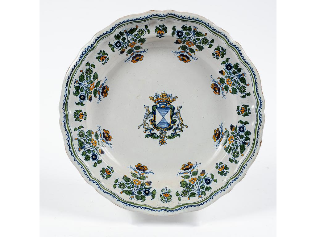 MOUSTIERS, XVIIIème siècle : Plat en faïence de Grand Feu, à riche décor polychrome aux armes de famille Blanc de Prunier, Dauphiné, dans un entourage de fleurs de solanacées. Diamètre : 29 cm