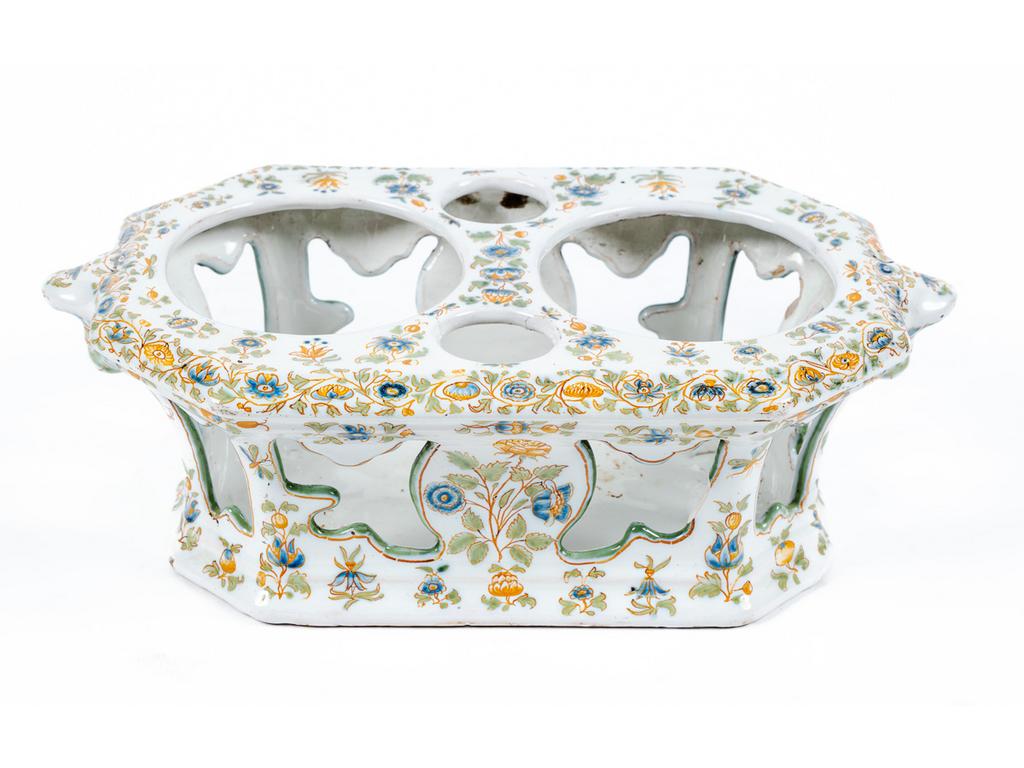 MOUSTIERS : Porte huilier-vinaigrier en faïence à décor polychrome de fleurs de solanacées. les côtés ornés de têtes d'indiens. Epoque XVIIIème siècle. Longueur : 26 cm.