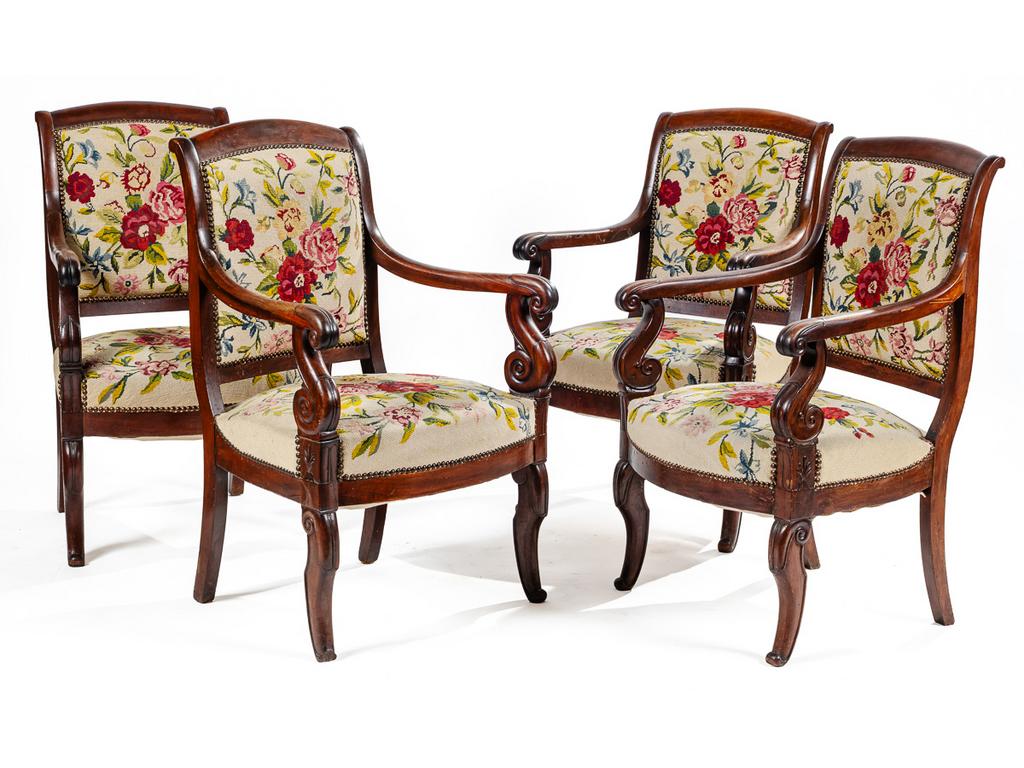 Suite de trois fauteuils d'époque Restauration en acajou et placage d'acajou ornés d'accotoirs à enroulement et reposant sur des pieds antérieurs jarrets. Garniture au point de croix à motif floral. (Reprise à un accotoir, doublure d'assise à reclouer). On y joint un fauteuil Restauration d'un modèle légèrement différent (Un bout de pied cassé).