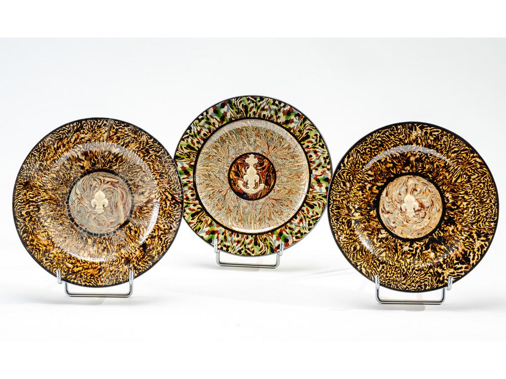 Manufacture PICHON à Uzès : Trois petites assiettes en céramique à décor de rosaces centrées d'une fleur de lys en relief sur fond marbré en terres mêlées. Deux signées du cachet de François PICHON. (Une avec petit manque et fêles de cuisson). Diamètres : 21,5 cm et 21 cm.