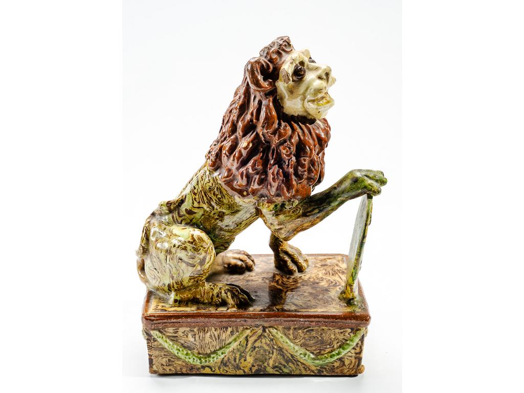 Manufacture PICHON à Uzès : Sujet en céramique à décor marbré en terres mêlées figurant un lion assis tenant un pavois, et reposant sur un socle à décor de guirlandes végétales. (Cassé, recollé, éclats). Dimensions : 25 x 17 x 10,5 cm.