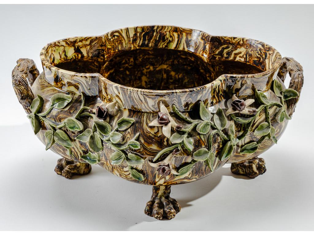 Manufacture PICHON à Uzès : Jardinière de table polylobée à anses, reposant sur quatre pieds griffes de lion et à décor, en relief, de fleurs et feuillages sur fond marbré en terres mêlées. Signée du cachet de François PICHON. (Petits manques et accidents au feuillage). Dimensions : 18 x 37 x 30 cm.
