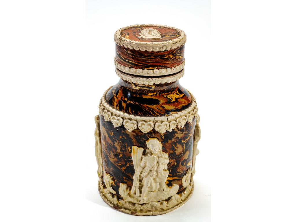 Manufacture PICHON à Uzès : Pot à tabac en céramique à décor, en relief, de personnages et rai de curs sur fond marbré en terres mêlées. Bouchon à vis orné d'un profil à l'antique. Signé du cachet de François PICHON sous la base et sous le bouchon intérieur. (Eclats au bouchon intérieur). Hauteur : 20 cm.