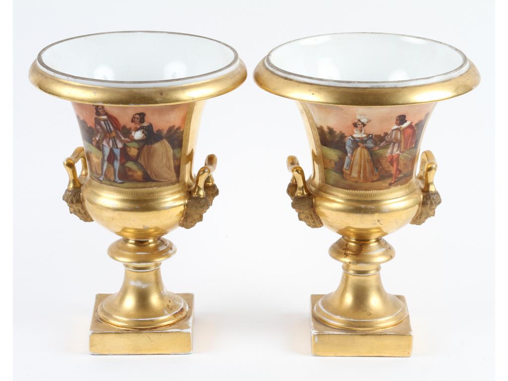 Paire de vases Médicis en porcelaine blanche entièrement dorée et bleue à décor peint de deux scènes romantiques. Petites anses à décor de mascarons. Epoque Restauration. (Usures à la dorure). Hauteurs : 27 cm.
