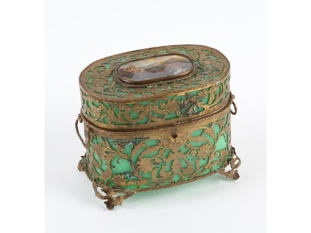 Coffret de forme ovale en opaline verte, sur une monture en laiton et tôle découpée de rinceaux feuillagés. Le couvercle orné d'une miniature peinte en fixé-sous-verre (altérations). (oxydations et infimes manques à la monture, sans la clé). Hauteur : 13 cm.