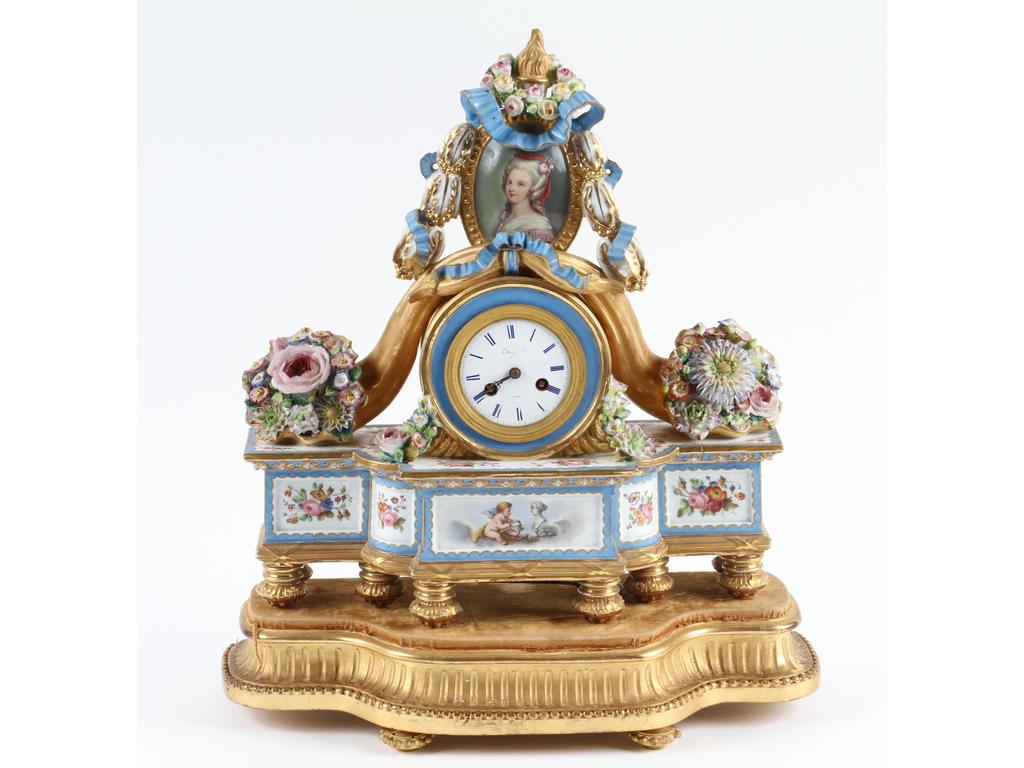 PARIS, Jacob PETIT : Pendule en porcelaine de style Louis XVI à décor peint de fleurs et d'un angelot artiste. Les côtés ornés de fleurs en relief et le sommet d'un médaillon rubané avec le portrait peint d'une femme. Marquée 