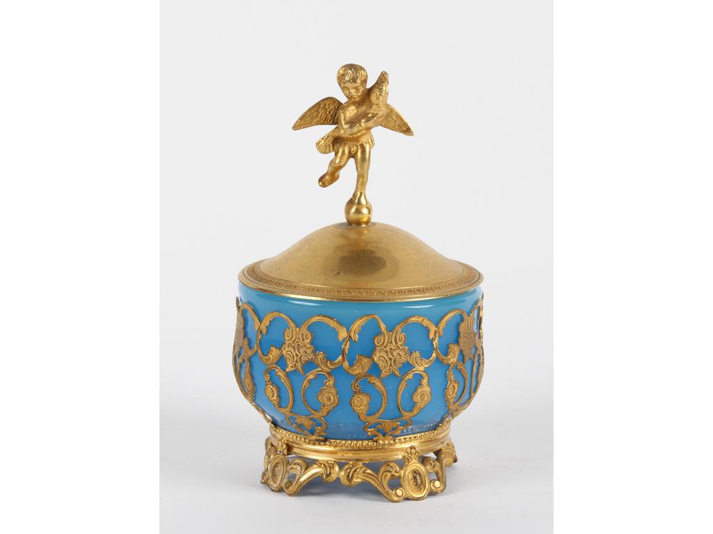 Petite boite ronde en opaline bleue sur une monture en laiton et tôle dorée. Le couvercle orné d'un angelot. Bon état. Hauteur : 12 cm.